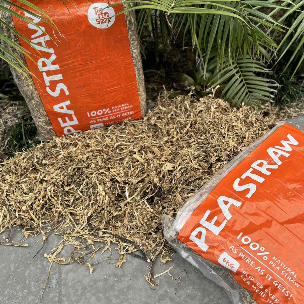 Two packages of Pea Straw with a small pile of straw on a stone surface.